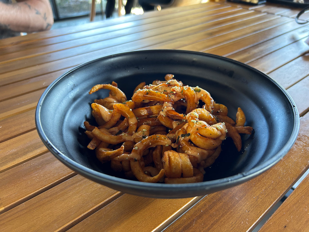 curly fries in a black plastic bowl on a wooden table